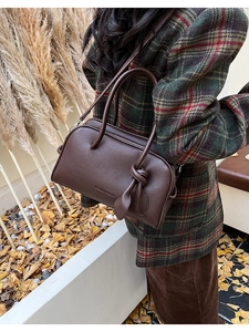 Detail der dunkelbraunen Boston-Tasche aus Leder mit Knotengriff auf einem Karomantel