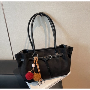 Close-up of black matte tote bag featuring a leather buckle and plush pom-pom charm