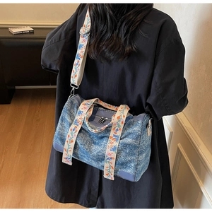 Detail of blue denim-textured Boston bag with floral strap on a black coat model