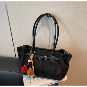 Detail of black suede tote bag with decorative strap and bicolor plush ball charm