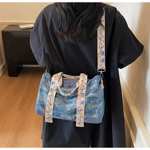 Detail of blue denim tote bag featuring floral embroidered straps and leather reinforced base
