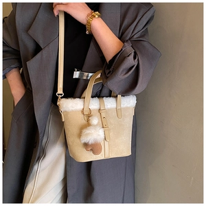 Detail of plush faux fur trim and heart charm on beige suede bucket bag for women