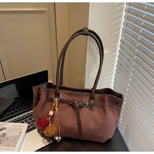 Detail of a dark brown suede tote bag featuring a plush charm and metal buckle detail