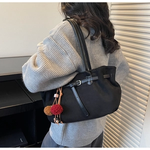 Detail of black tote bag featuring leather straps and decorative dual-tone pompom charms