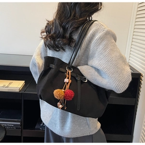 Detail of black suede-textured tote bag with colorful plush ball charm and drawstring detail
