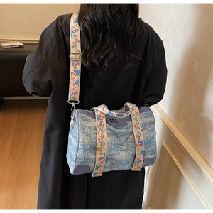 Detail of blue denim cylinder bag with colorful floral embroidered wide shoulder strap