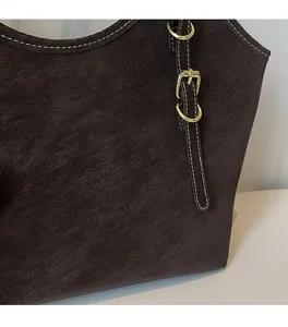 Close-up of brown textured leather tote with white contrast stitching and gold buckle