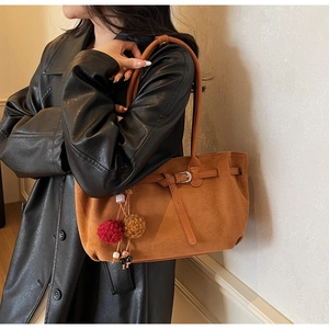 Detailed texture of brown faux suede tote bag with decorative buckle and plush charms