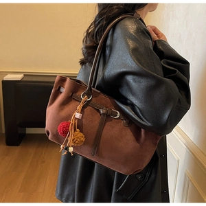 Detail view of brown suede tote bag with decorative metal buckle and plush pompom charm