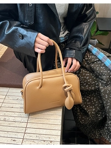 Detail von Knotengriff und Lychee-Struktur auf brauner Tasche mit Fashion-Logo