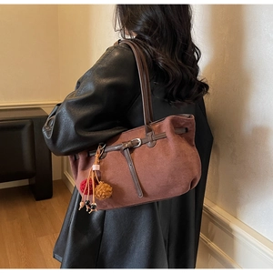 Detail of vintage brown suede tote bag with plush pom-pom charm on female model