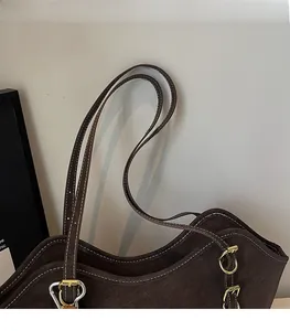 Detail of brown suede tote bag featuring white contrast stitching and gold metal buckles