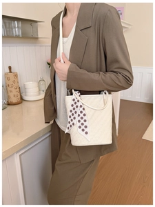 Sac seau tissé beige chic avec détail foulard à pois marron porté par un mannequin