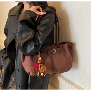 Detail of dark brown suede tote bag with leather strap buckle and colorful plush charms