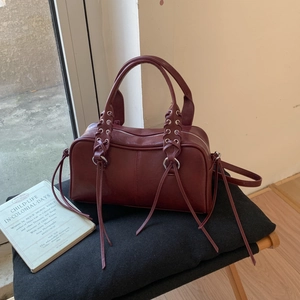 Vue détaillée du sac bowling bordeaux en cuir avec pompons sur une chaise vintage