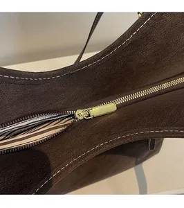 Detailed close-up of premium gold zipper and striped lining on dark brown leather tote bag