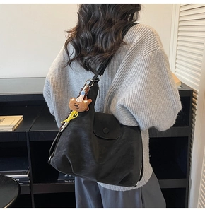 Detail of a large black tote bag with a brown bear plush charm on a model's shoulder