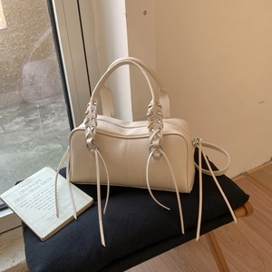 Détail du sac Boston crème avec poignées tressées et franges latérales sur un siège