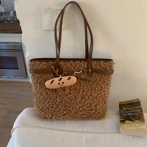 Detail of a brown fuzzy tote bag with leather handles and a baguette plush keychain