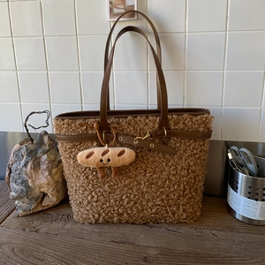 Detail of plush brown tote bag with leather handles and cute bread-shaped charm