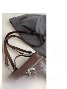 Detail of brown crocodile pattern handbag with adjustable strap and silver zipper