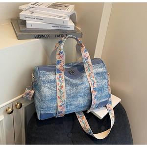 Detail of blue denim Boston bag featuring floral embroidery on the cream webbing strap