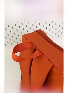 Detail of burnt orange nylon backpack with reinforced handle and sturdy zipper closure