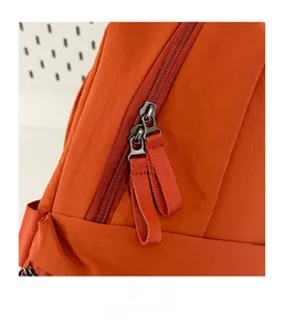 Detail view of smooth metal zippers and durable orange nylon fabric on travel backpack