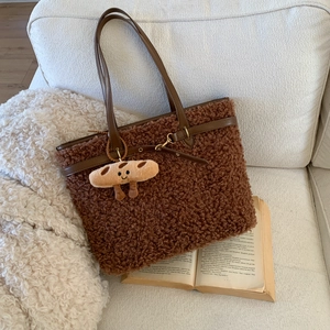 Close-up of brown plush tote bag with leather straps and a cute cartoon charm on a sofa