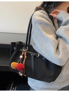 Minimalist black tote bag with colorful pompom charm shown on a female model
