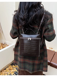Detail of dark brown faux crocodile leather backpack worn with a plaid wool coat