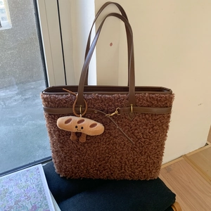 Detail of dark brown faux shearling tote bag with leather handles and bread charm