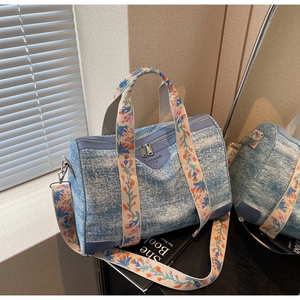 Close-up of denim blue Boston bag with floral woven straps and silver hardware detail