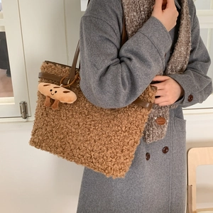 Detail of a brown faux shearling tote bag with leather handles and a plush bread charm
