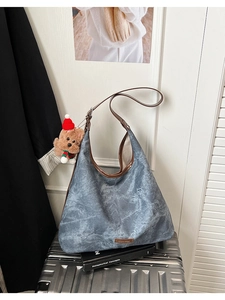 Detail of blue denim tote bag with brown leather trim and cute bear charm on suitcase