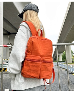 Street style shot of a bright orange lightweight backpack with multiple zipper pockets