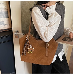 Close-up of brown suede tote bag with cute bear charm shown on model's shoulder