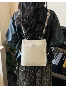 Detail of beige crocodile pattern backpack with silver zipper and metallic strap hooks