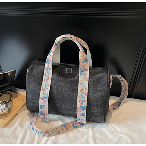 Detail view of dark denim boston bag with floral embroidered straps and leather patch