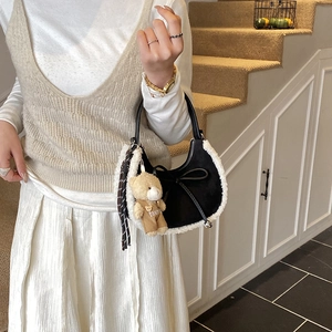 Détail du sac à main noir en daim avec bordure en fausse fourrure et breloque d'ours