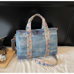 Detail of blue denim tote bag featuring colorful floral embroidered wide straps and handles