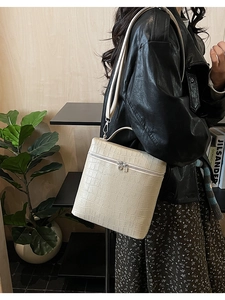 Detail view of beige crocodile embossed bucket bag with gold zipper and dual straps