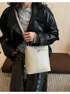 Close-up of beige crocodile texture crossbody bag with gold zippers on model outfit