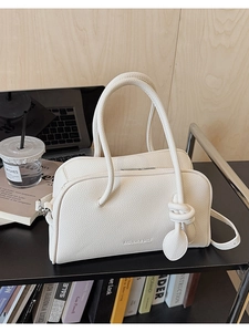 Dettaglio della trama in pelle color crema della borsa con ciondolo a nodo su un tavolo