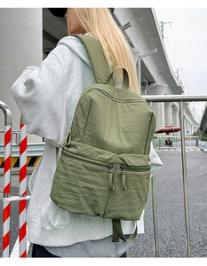 Olive green nylon backpack with multiple zipper pockets shown from the back during outdoor use