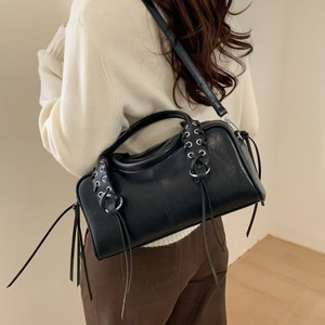 Détail du sac cylindrique en cuir noir avec œillets argentés et longs glands porté en bandoulière