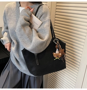 Detail of black tote bag featuring white contrast stitching and cute bear charm accent