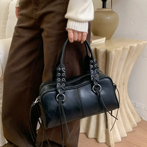 Détail d'un sac cabas en cuir noir avec poignée tressée, oillets métalliques et pompons