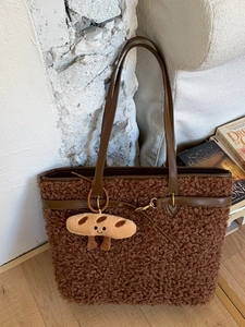 Brown faux fur tote bag with leather straps and cute baguette charm in home setting