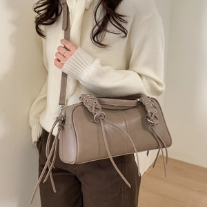 Détail du sac cylindre taupe avec poignée tressée, pompons décoratifs et anneaux argent